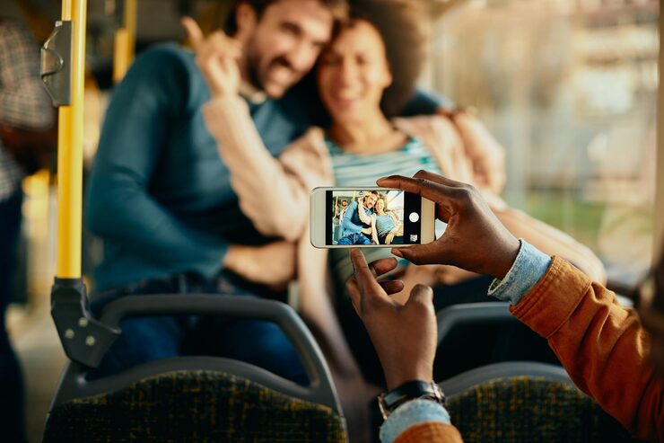 Closeup of a man photographing happy couple with cell phone in a bus