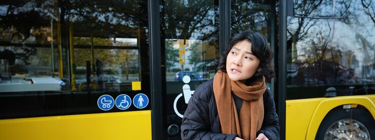 Korean girl in winter clothes waits for her bus on stop looking for her transport holding mobile