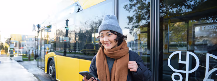 Portrait of girl standing near bus on a stop waiting for her public transport schecks schedule on
