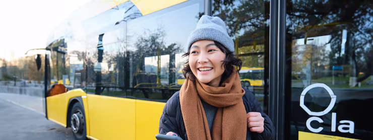 Portrait of girl standing near bus on a stop waiting for her public transport schecks schedule on